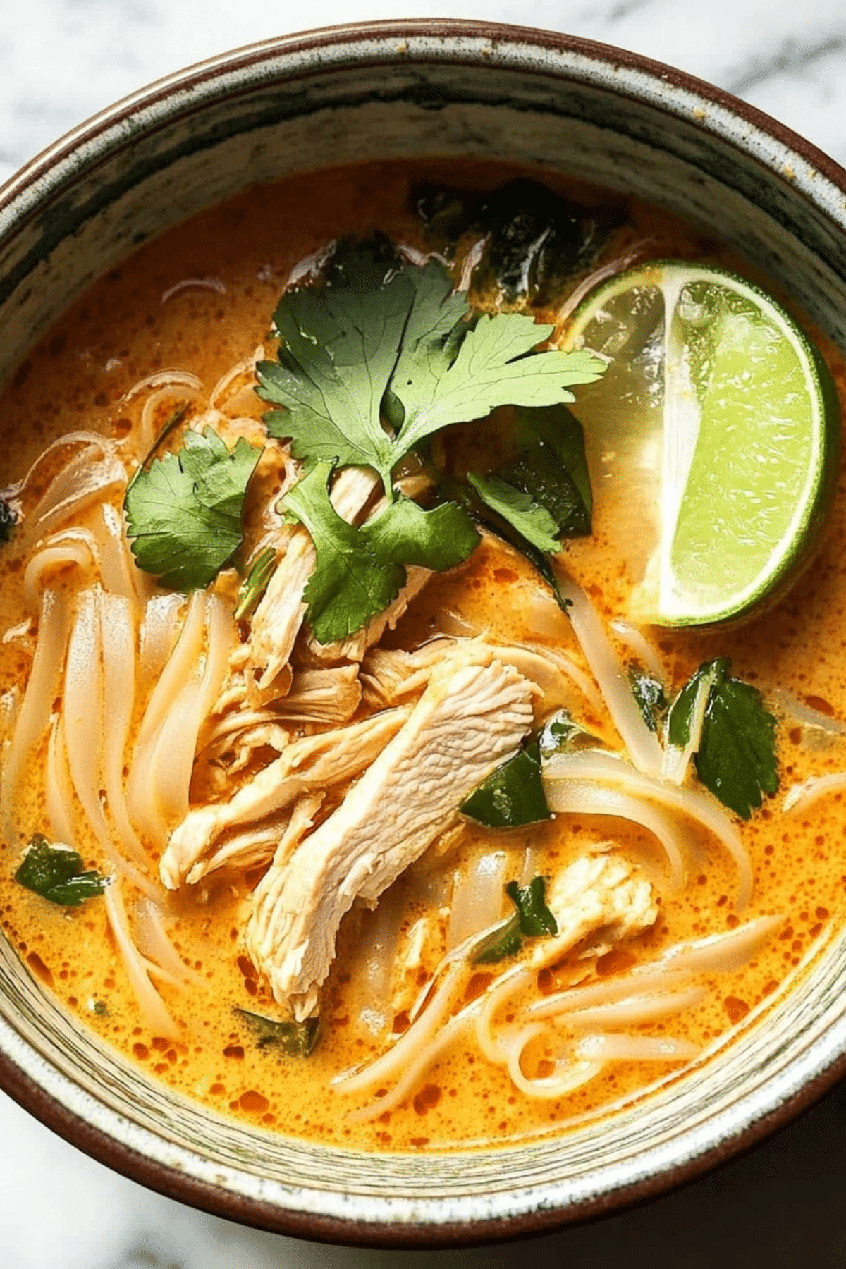 bowl of thai chicken curry soup with noodles and fresh herbs