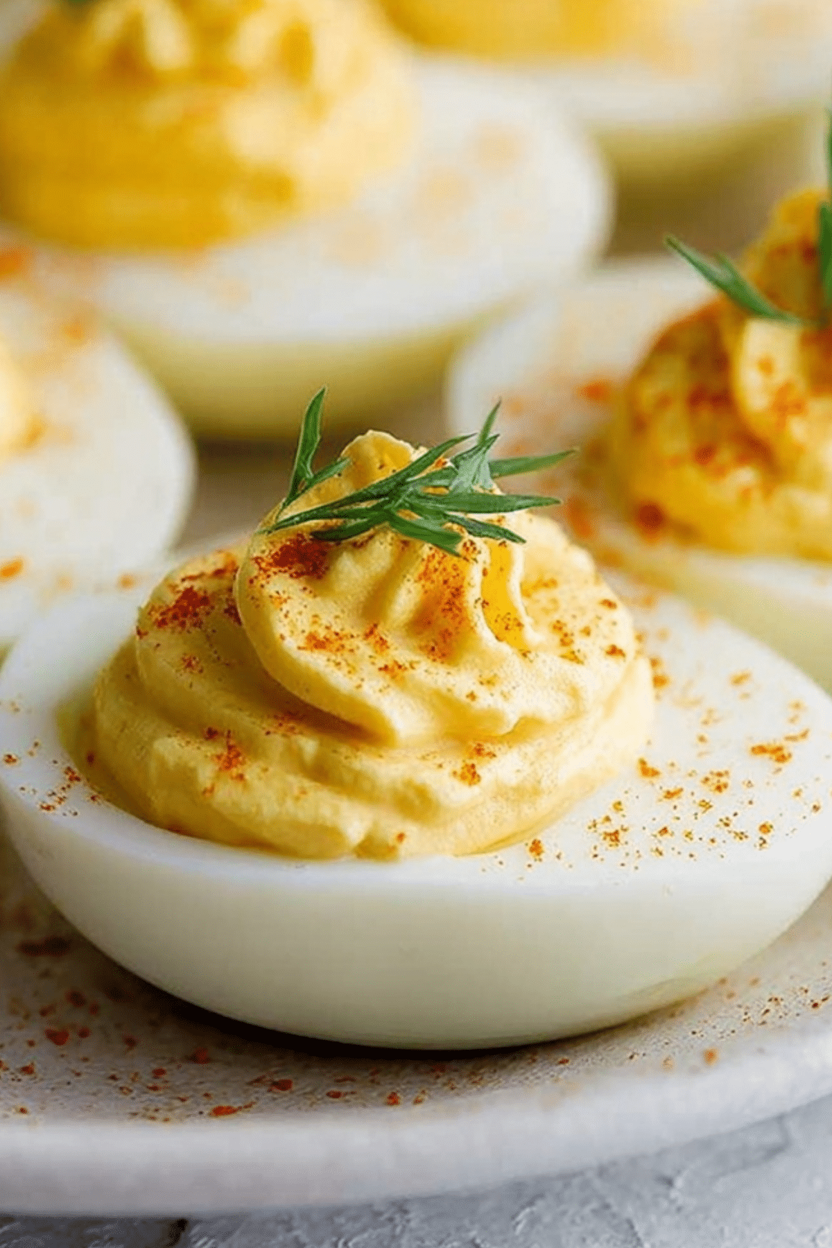 Classic Deviled Eggs on white platter with paprika and herbs