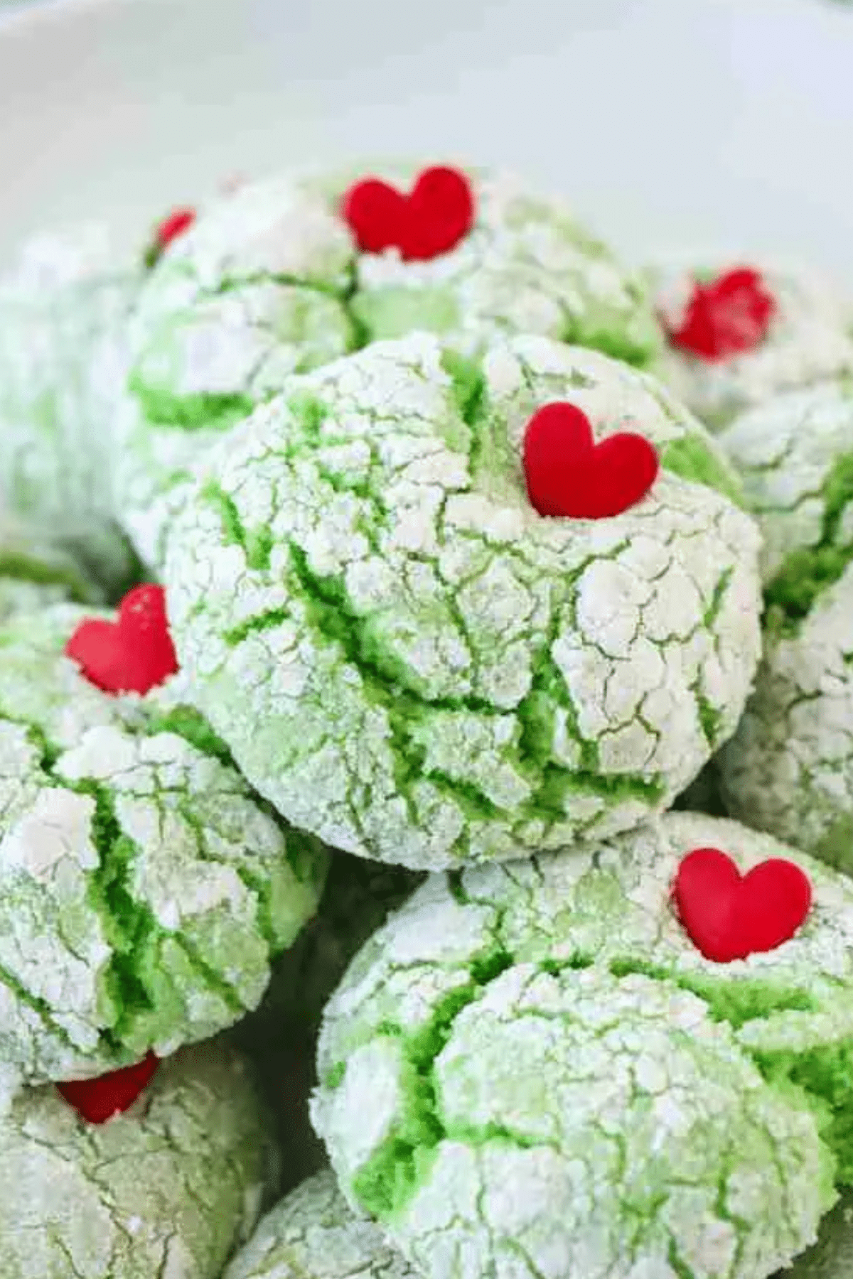 Grinch cookie recipe featuring green crinkle cookies with red heart sprinkles