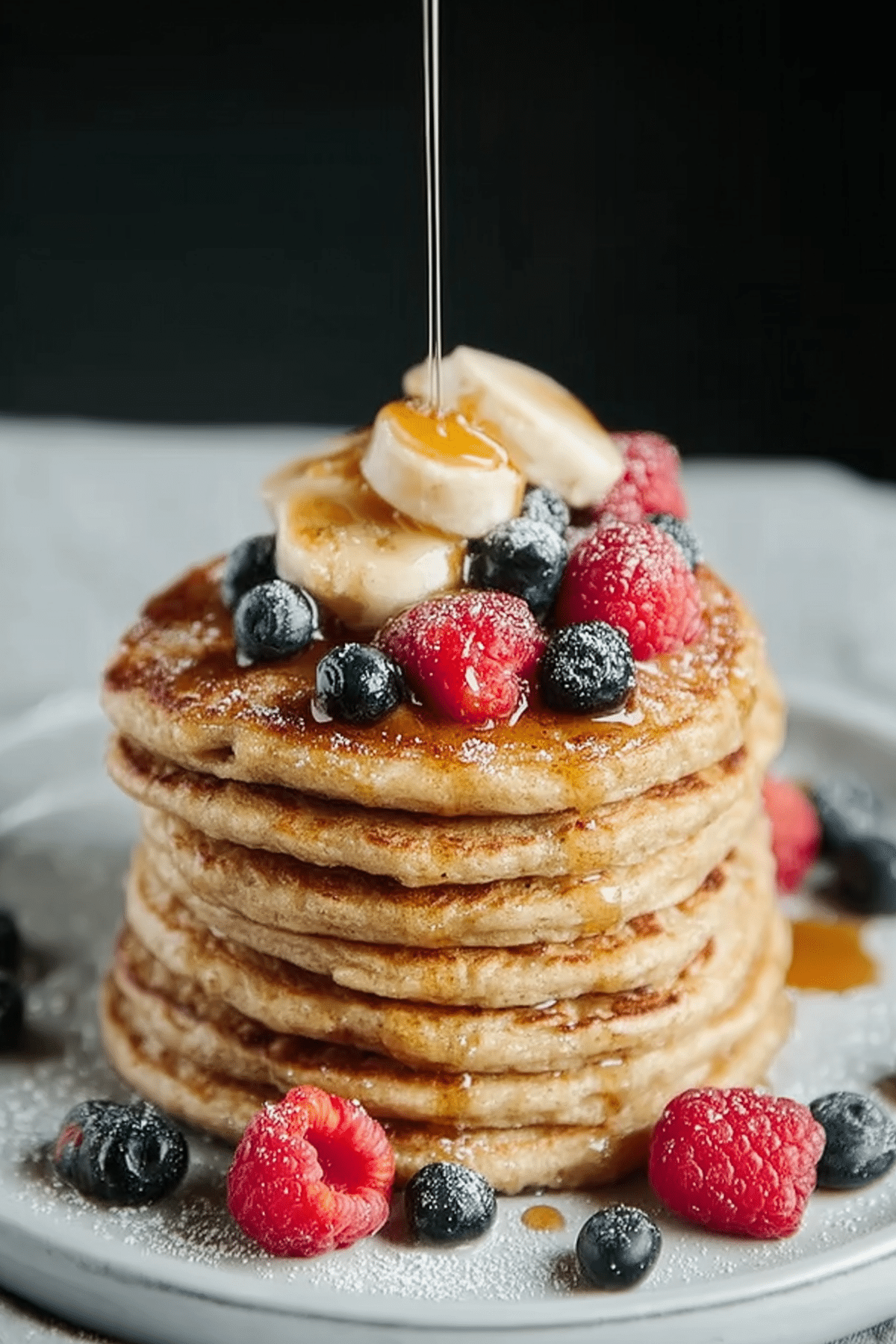 Cottage Cheese Banana Oatmeal Protein Pancakes stacked on a plate with fresh fruit